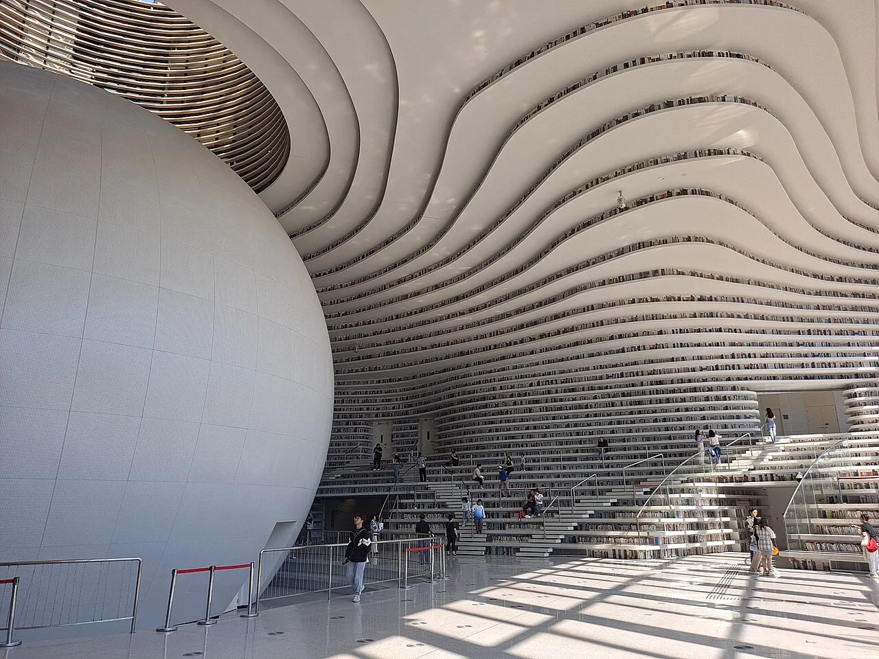 The curving white bookshelves and spherical auditorium inside Tianjin Binhai Library